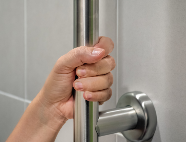 Close up image of someone holding on to a handrail installed in a bathroom